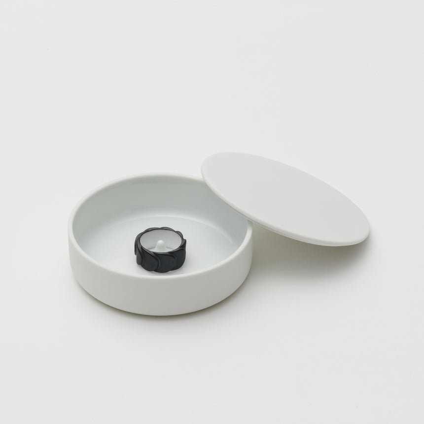 White porcelain jewelry holder designed by Saskia Diez for Arita 2016. Handmade in Japan. Glazed interior, matte exterior. Water drop detail in middle with thin walled lid leaning on side of base. Black ring inside.
