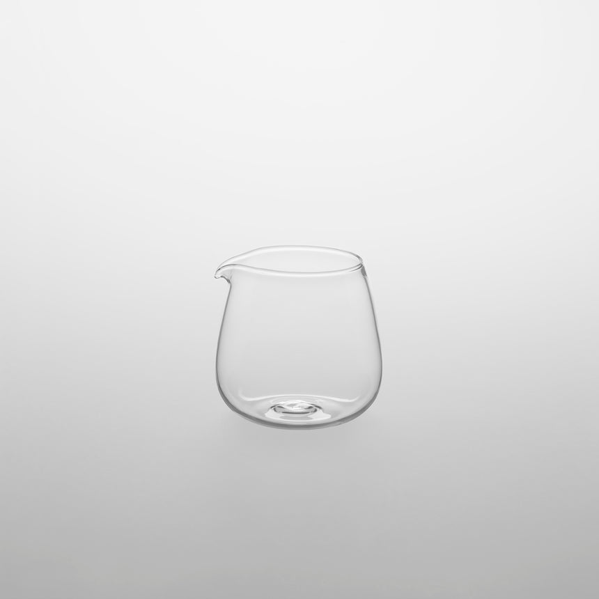 Small clear glass milk creamer with spout. Designed by Naoto Fukasawa for TG Taiwan Glass. Clear borosilicate on grey background.