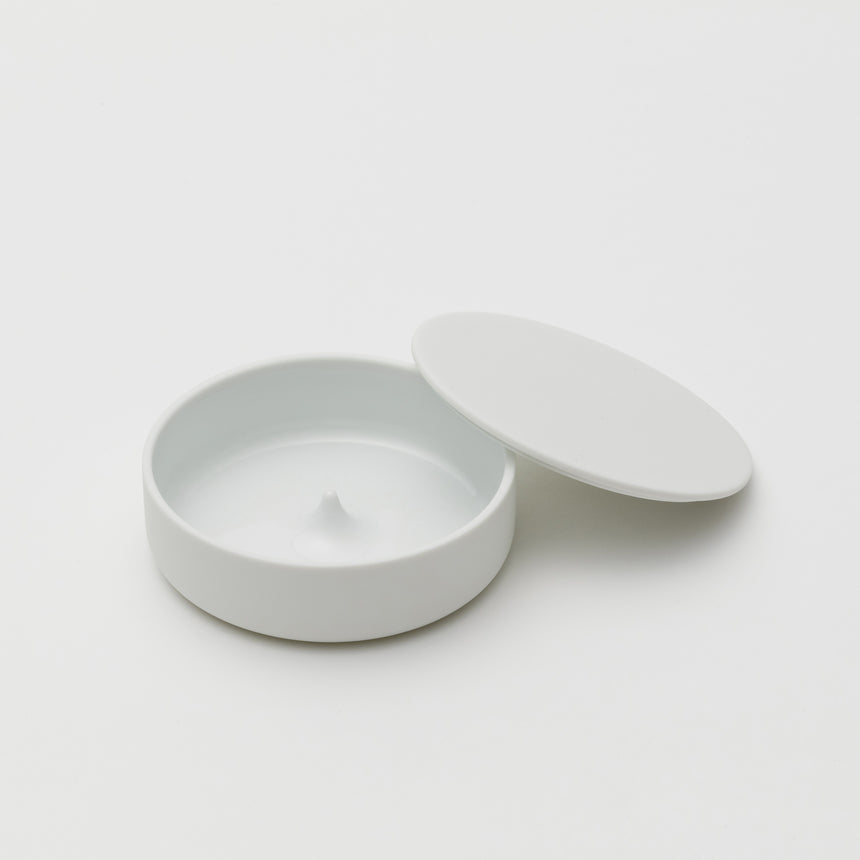 White porcelain jewelry holder designed by Saskia Diez for Arita 2016. Handmade in Japan. Glazed interior, matte exterior. Water drop detail in middle with thin walled lid leaning on side of base.