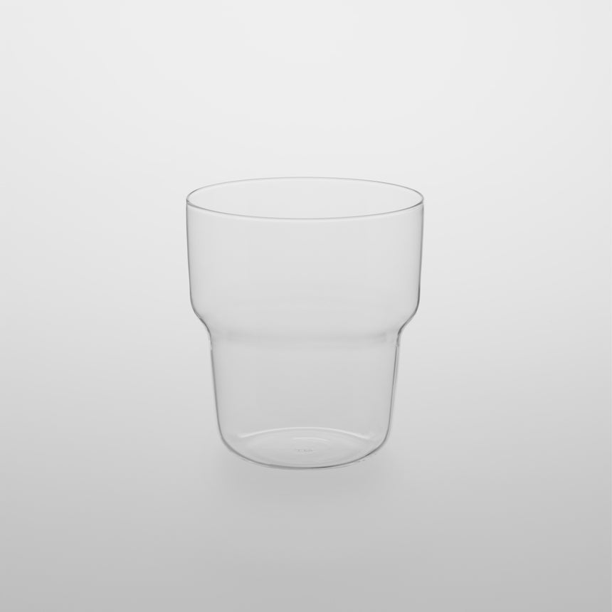 Small stackable curved glass tumbler cup. Designed by Naoto Fukasawa for TG Taiwan Glass. Clear borosilicate on grey background.