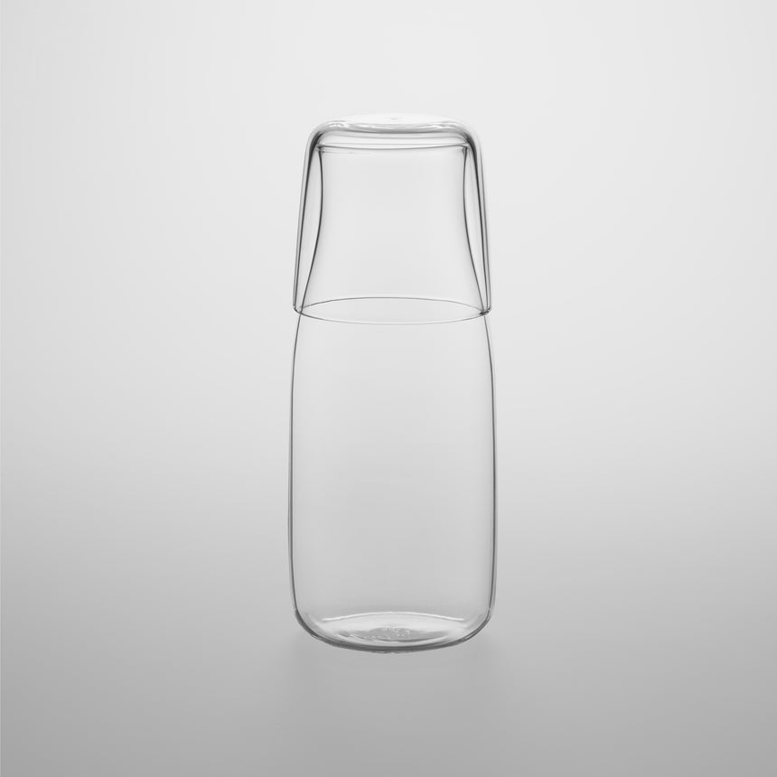 Glass pitcher with fitted cup Designed by Naoto Fukasawa for TG Taiwan Glass. Clear borosilicate on grey background. Cup is on top of pitcher.